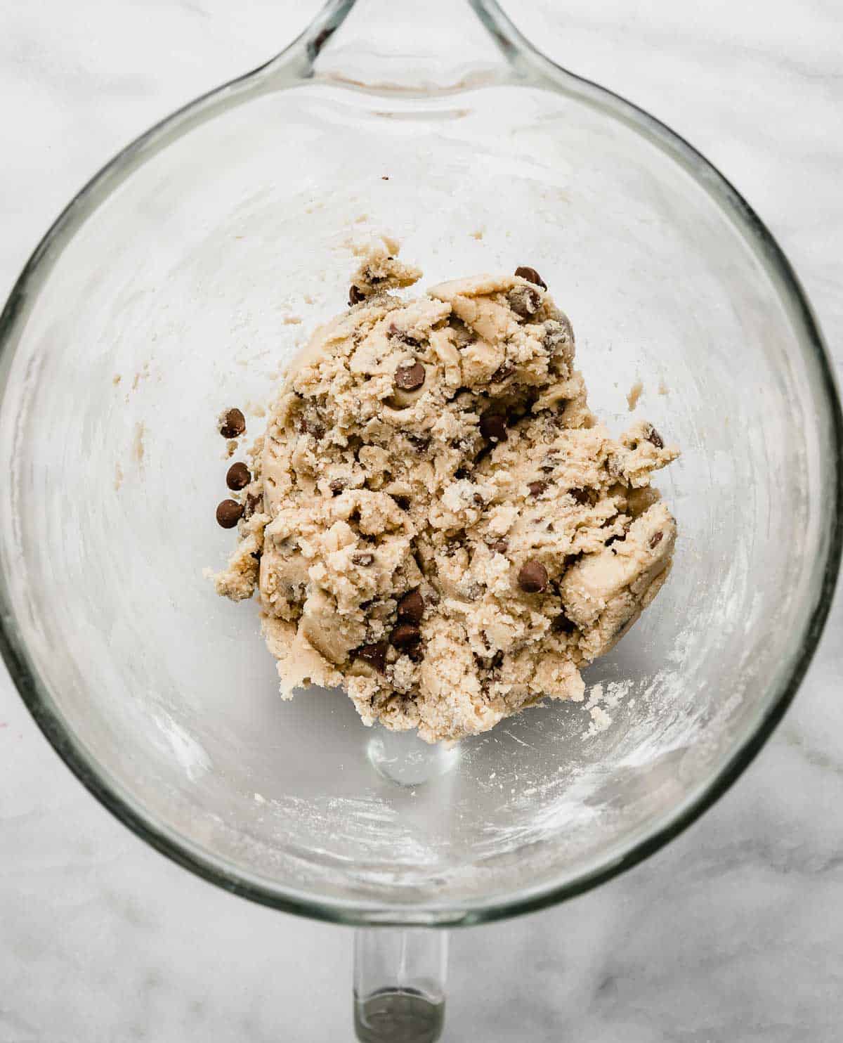 Milk Chocolate Chip Cookie dough in a glass stand mixer bowl on a white background.