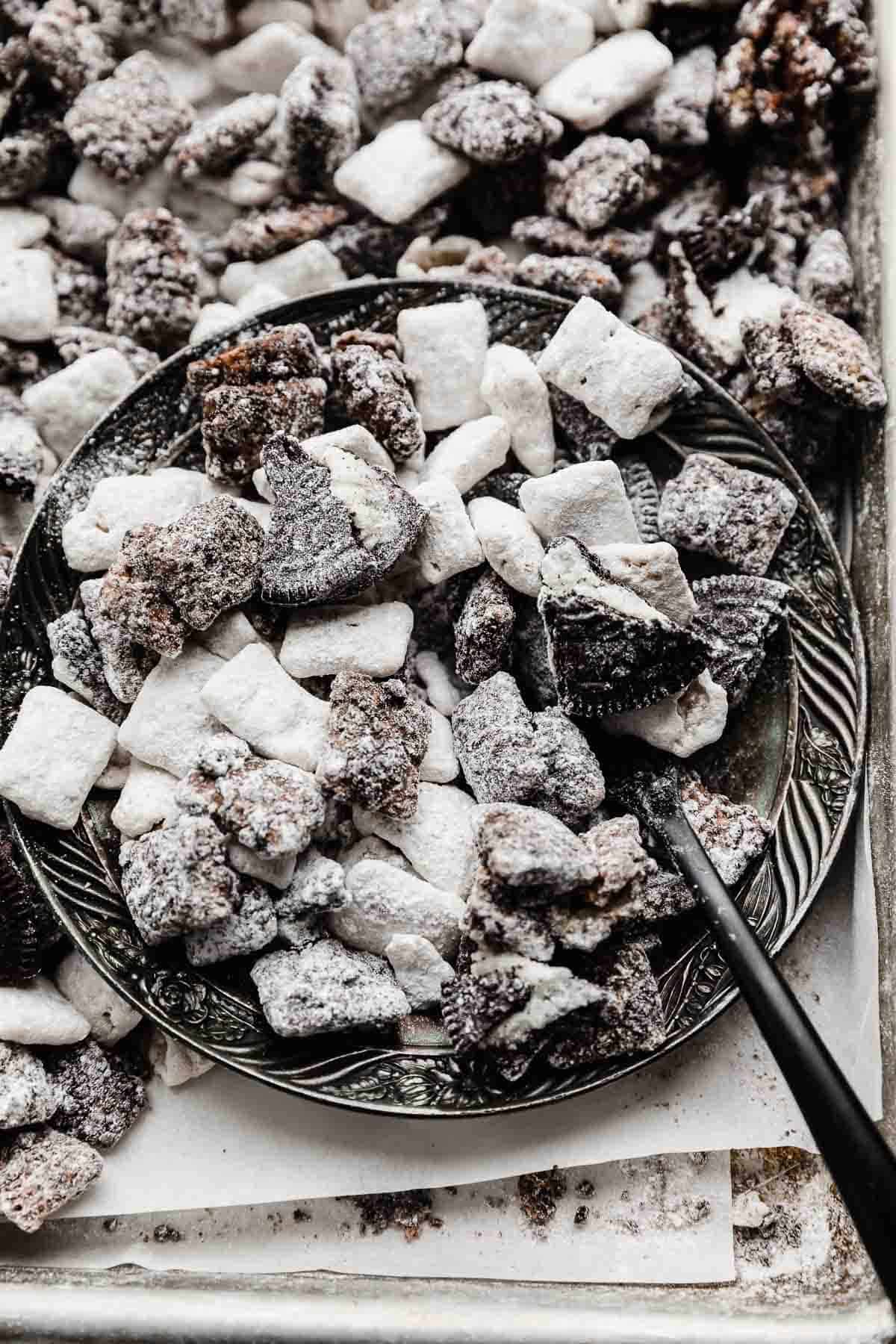 Oreo Muddy Buddies on a silver plate surrounded by additional cookies and cream puppy chow.