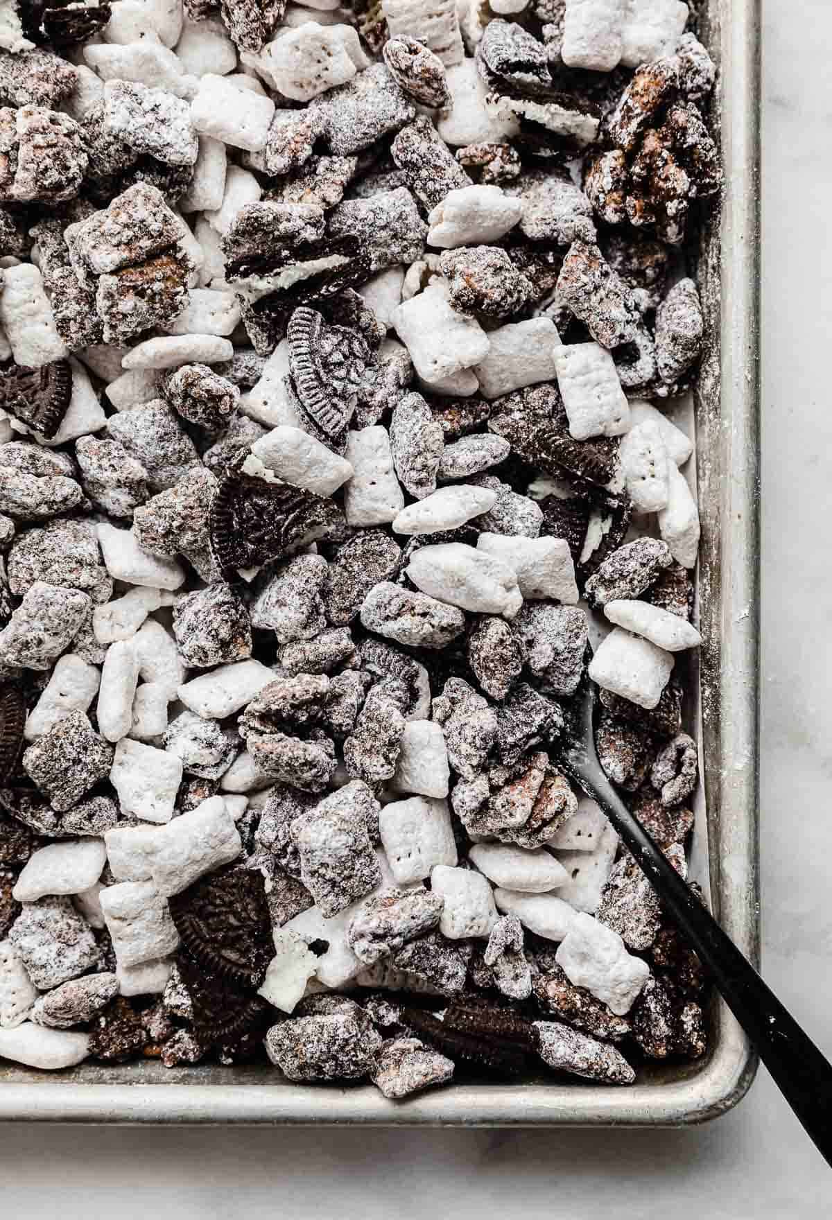 Oreo Muddy Buddies on a baking sheet with a black spoon scooping up some of the Oreo puppy chow.