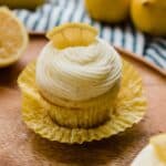 Lemon Cupcake topped with a swirl of lemon frosting and a lemon wedge on a brown background.