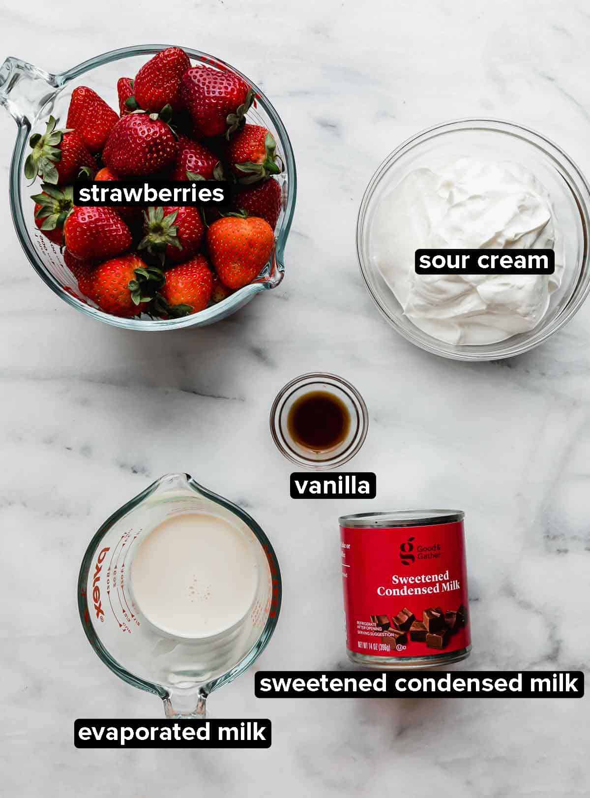 Strawberries and Cream (Fresas con Crema) recipe ingredients portioned into glass bowls on a white and gray marbled background.