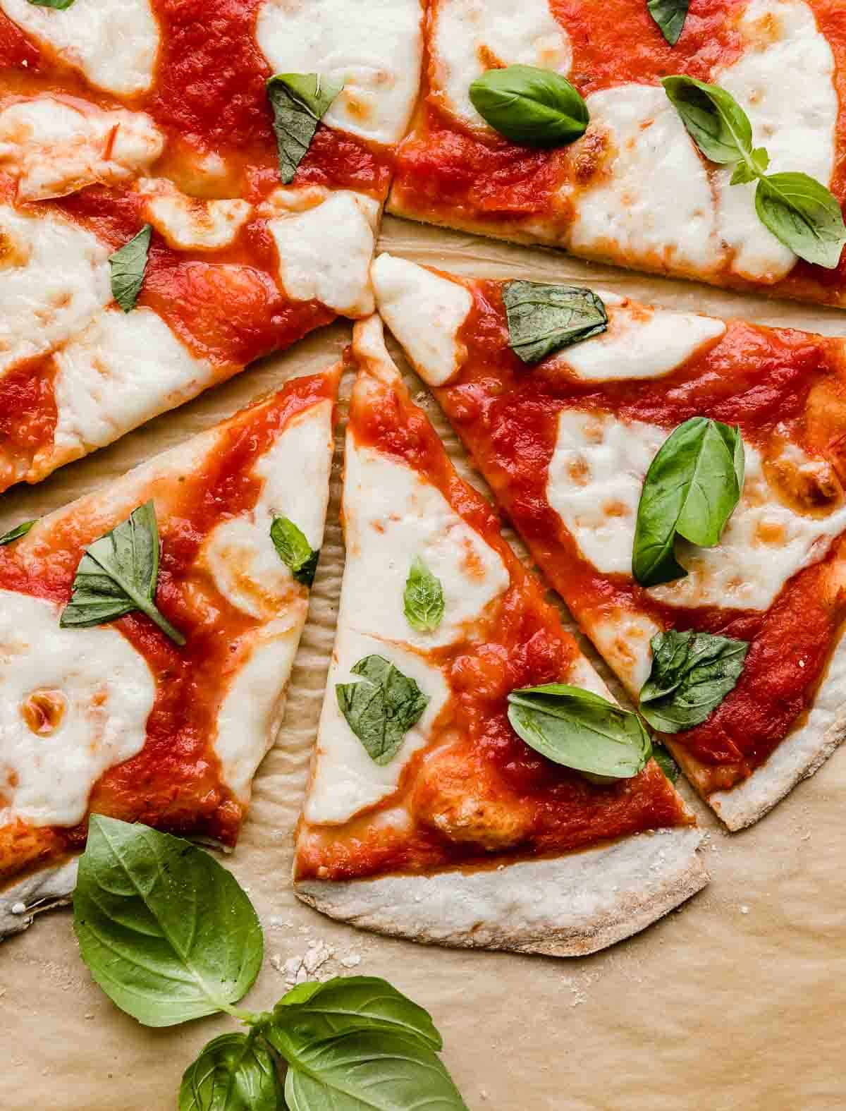 Several slices of Authentic Margherita Pizza topped with fresh basil on a Kraft parchment paper.