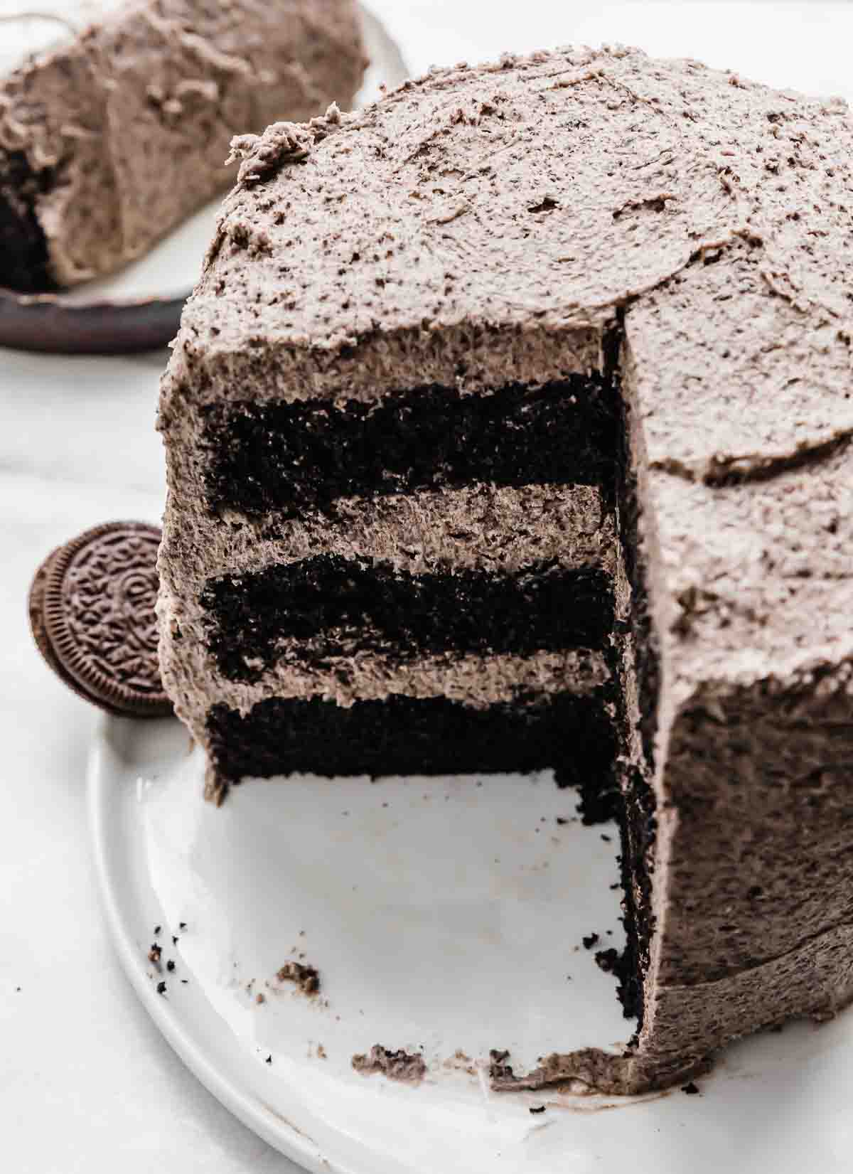 An Oreo Cake recipe on a white plate with a fourth of the cake cut from the main cake.