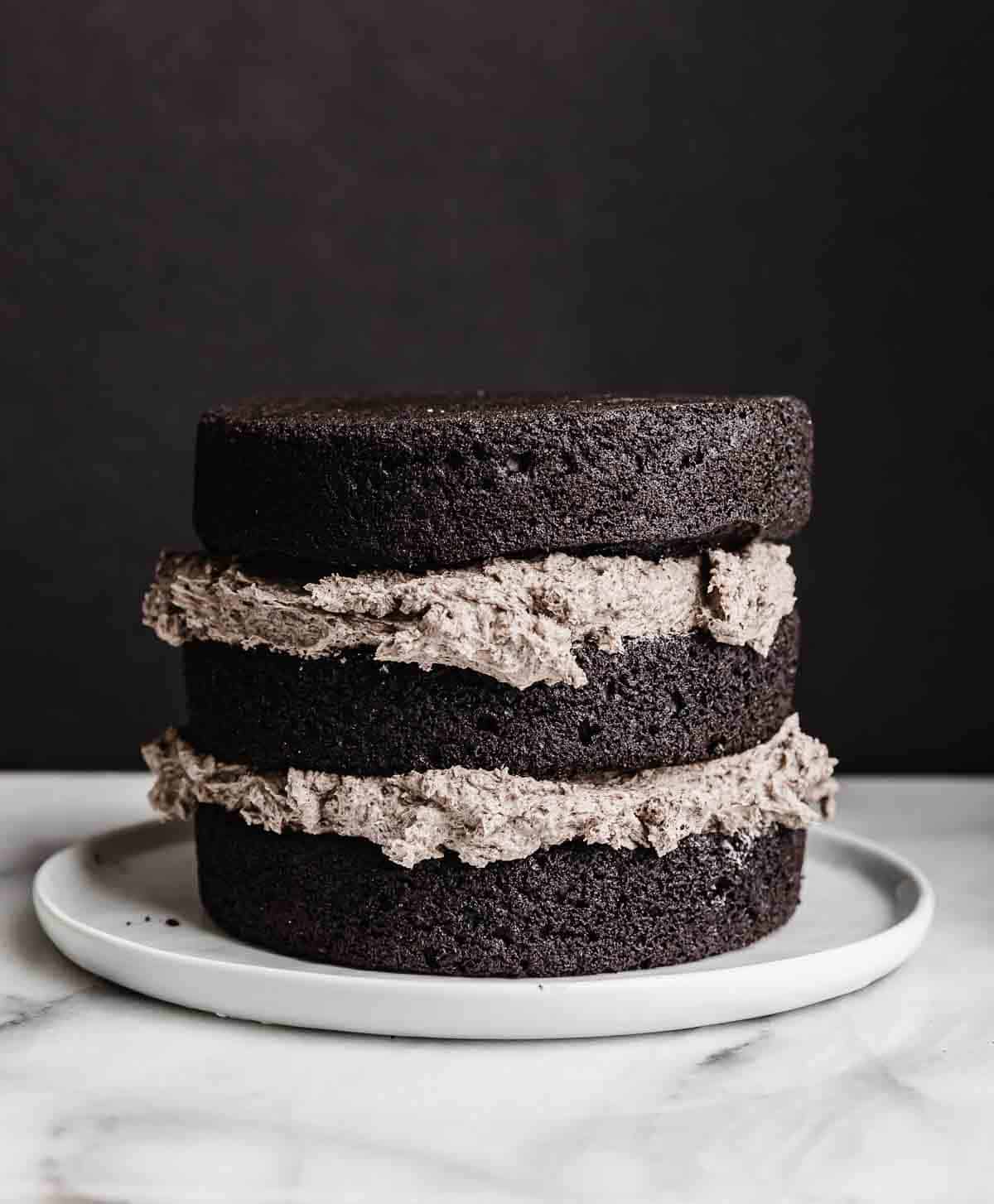 A three layer black cocoa cake with Oreo frosting between each cake layer, against a white background.