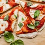 Authentic Margherita Pizza topped with fresh mozzarella and torn fresh basil on a light brown parchment paper.