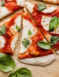 Authentic Margherita Pizza topped with fresh mozzarella and torn fresh basil on a light brown parchment paper.