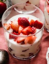 A glass cup filled with Strawberries and Cream (Fresas con Crema) on a red linen background.