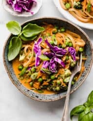 A blue bowl filled with Coconut Curry Noodles and vegetables topped with basil and purple cabbage.