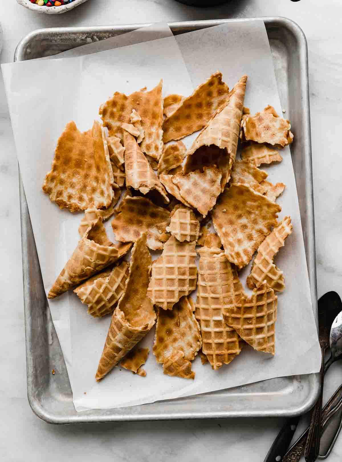 Broken waffle cones on a white parchment lined baking sheet on a white background.