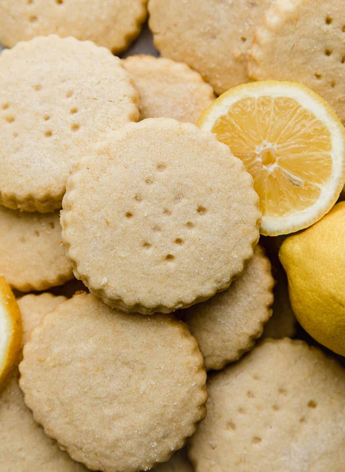 A close up photo of Lemon Shortbread Cookies stacked on top of each other, with a lemon slice to the right of the cookies.