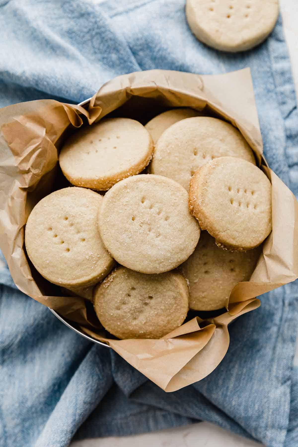 Overhead photo of Grandma's Shortbread Cookies (cut into round circles) in a round tin on a light blue napkin.