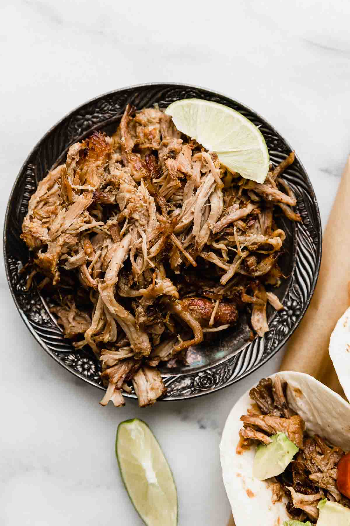 Slow cooker Mexican shredded pork on a black plate on a white background.