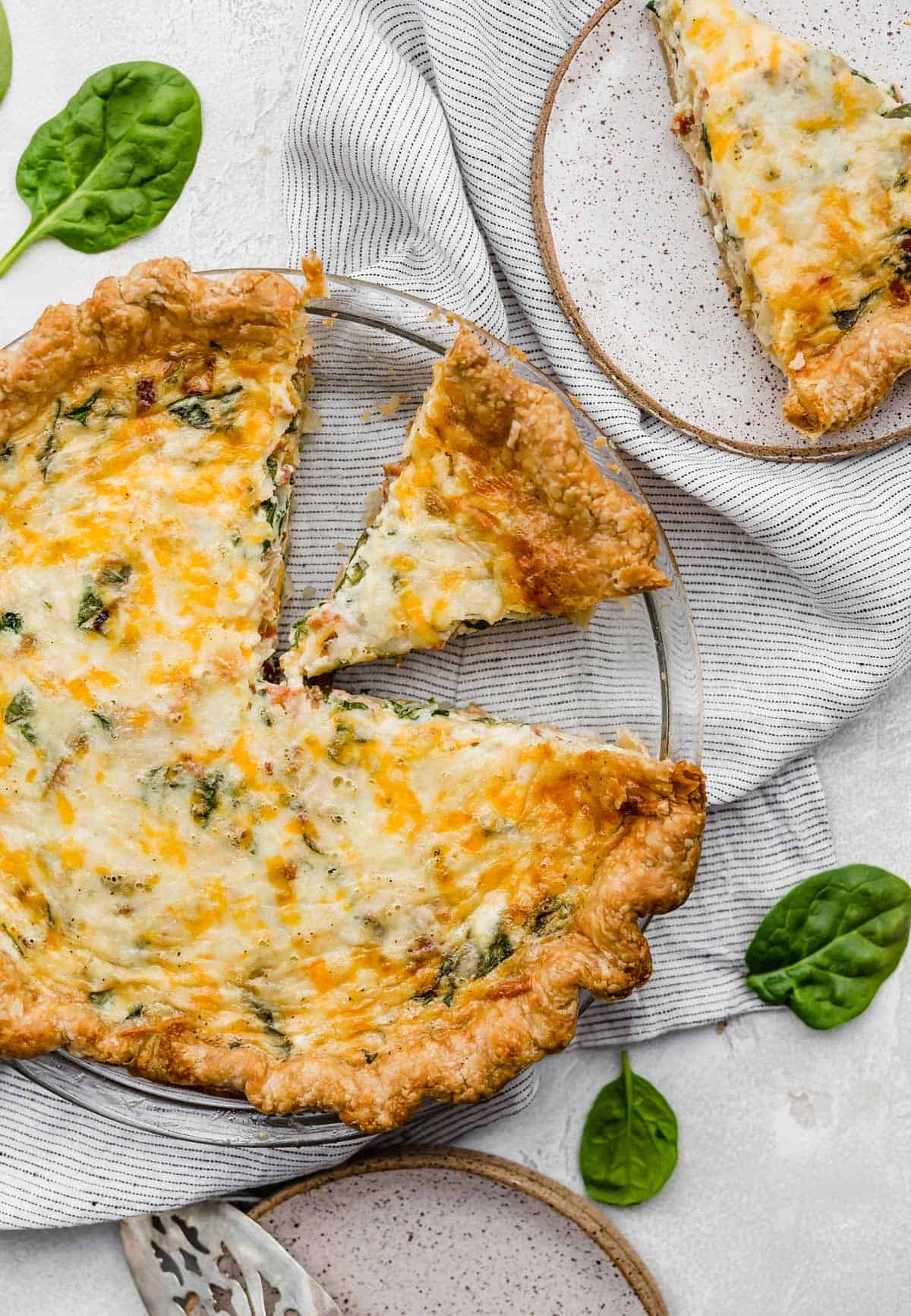 A picture showing a delicious spinach and bacon quiche with a slice cut out.