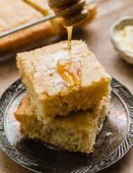 Honey being drizzled over a square slice of Bisquick Cornbread that's on a tarnished plate.