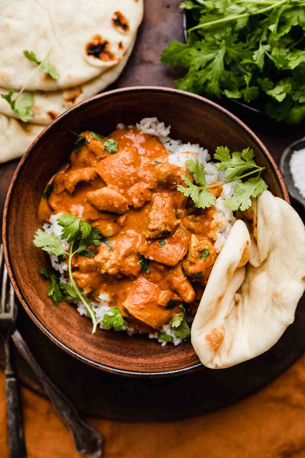 Chicken Tikka Masala in a brown bowl garnished with cilantro and a side of naan bread.