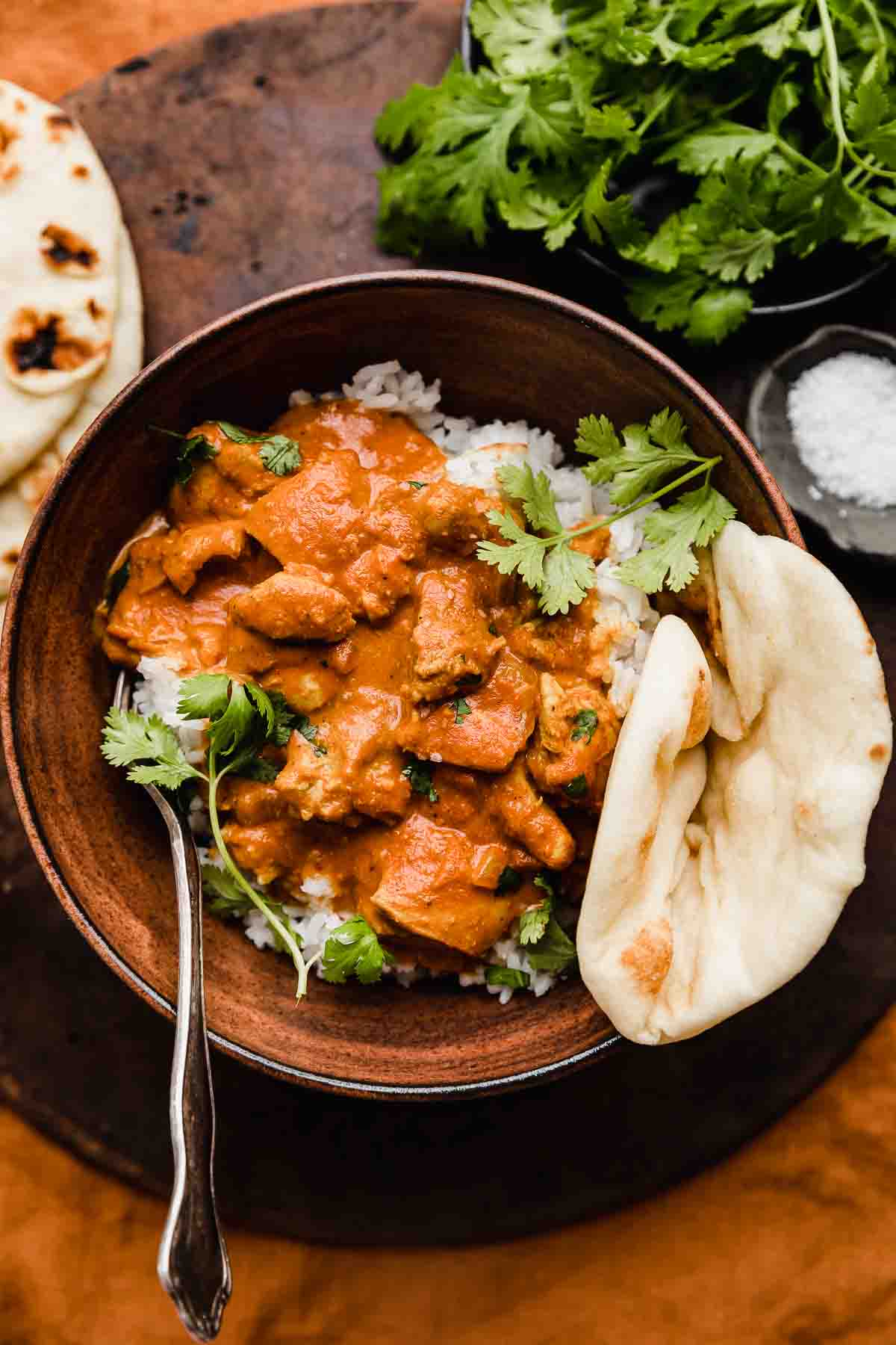 Chicken Tikka Masala recipe overtop rice with a side of naan, on a brown and deep orange colored background.