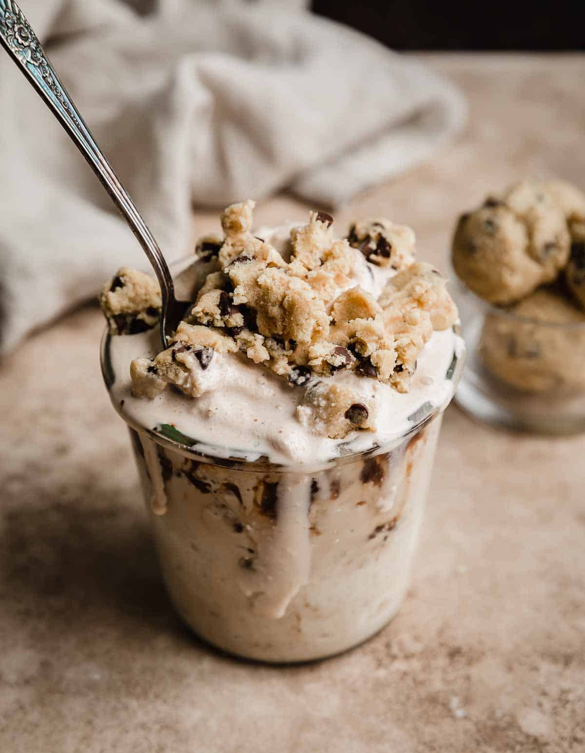 Chocolate Chip Cookie Dough Blizzard topped with cookie dough chunks in a glass cup on a light brown background.