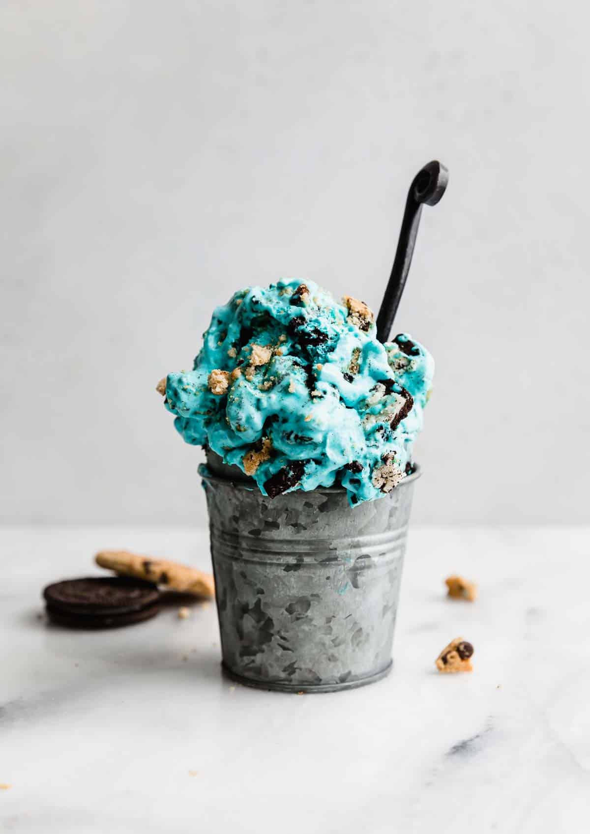 A metal cup filled with Cookie Monster Ice Cream against a white background.