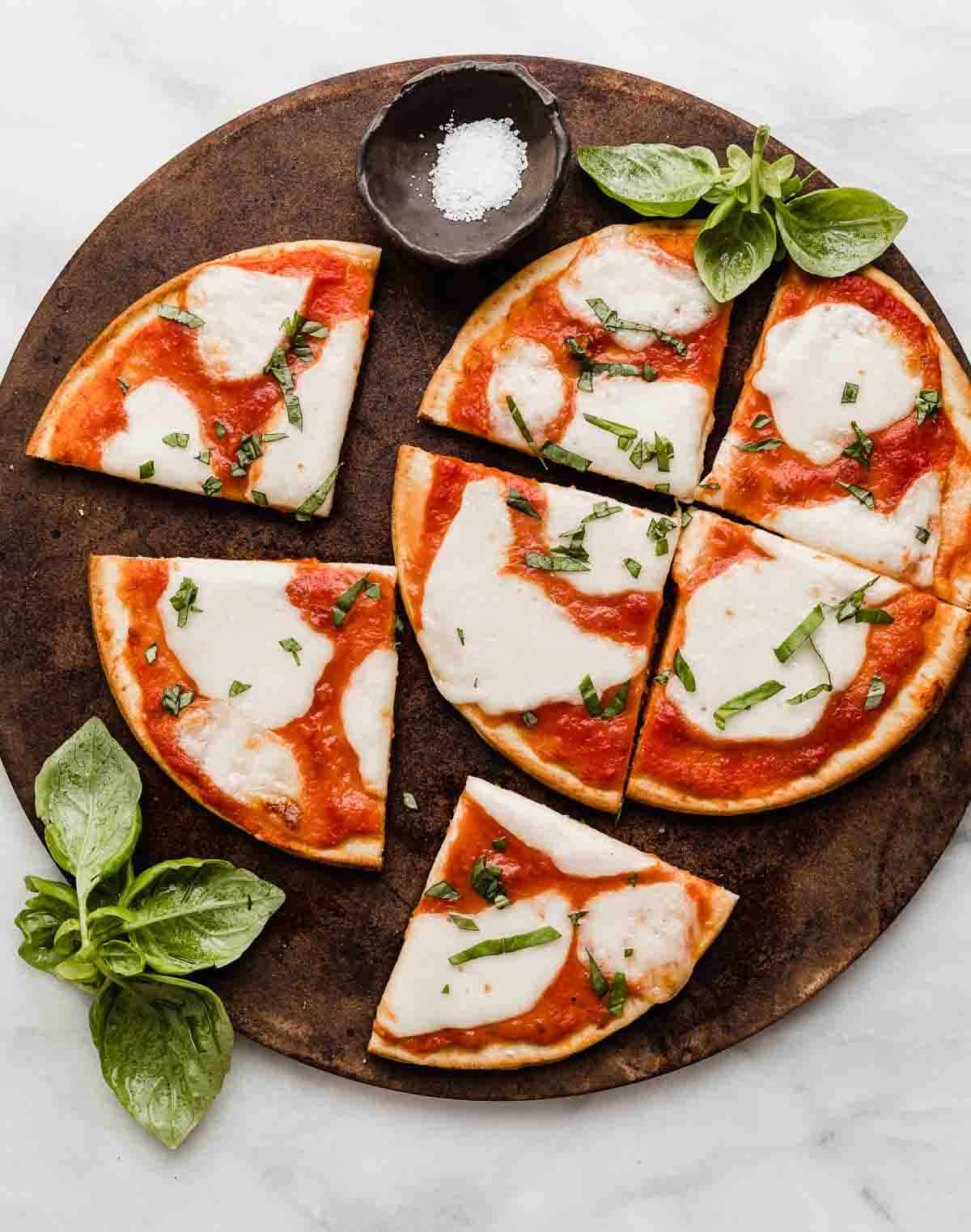 Margherita Flatbread pizza on a brown pizza stone that's on a white marble table.