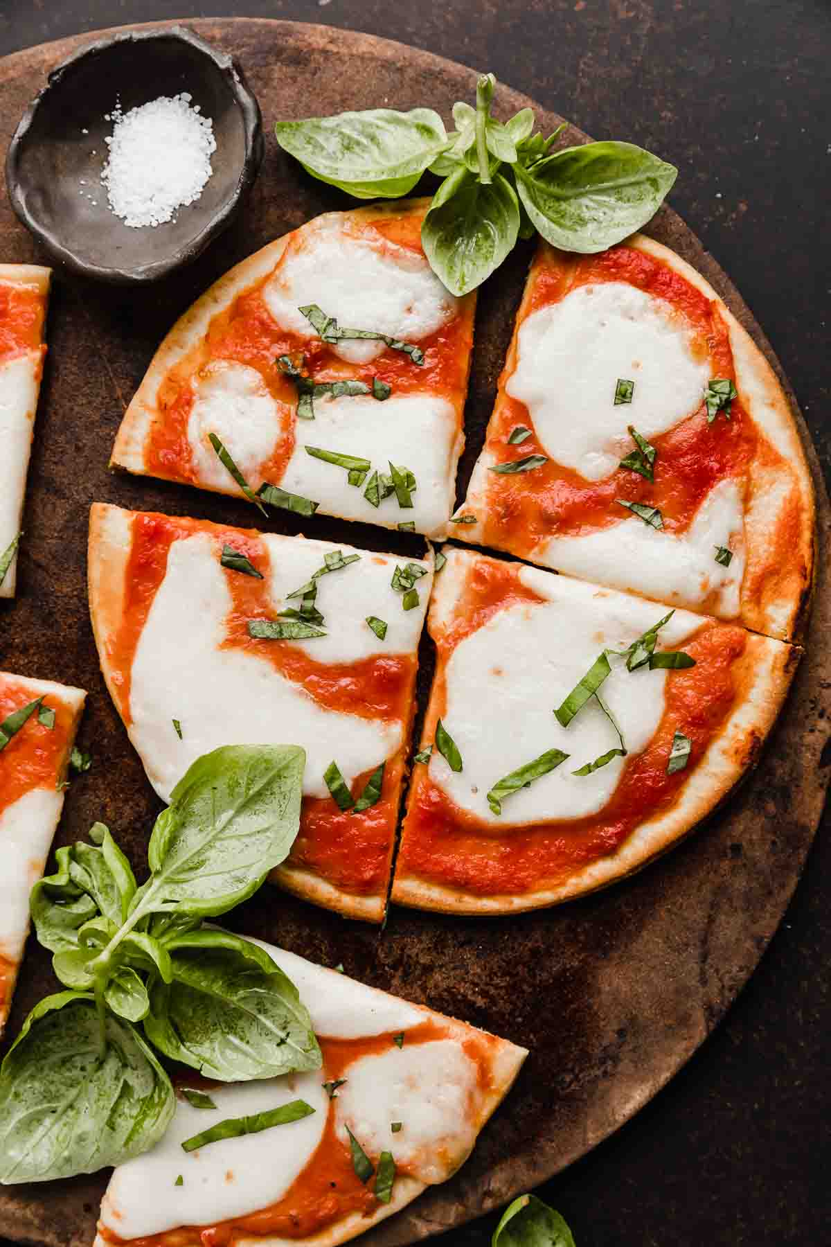 A Margherita Flatbread pizza topped with fresh basil, on a round pizza stone.