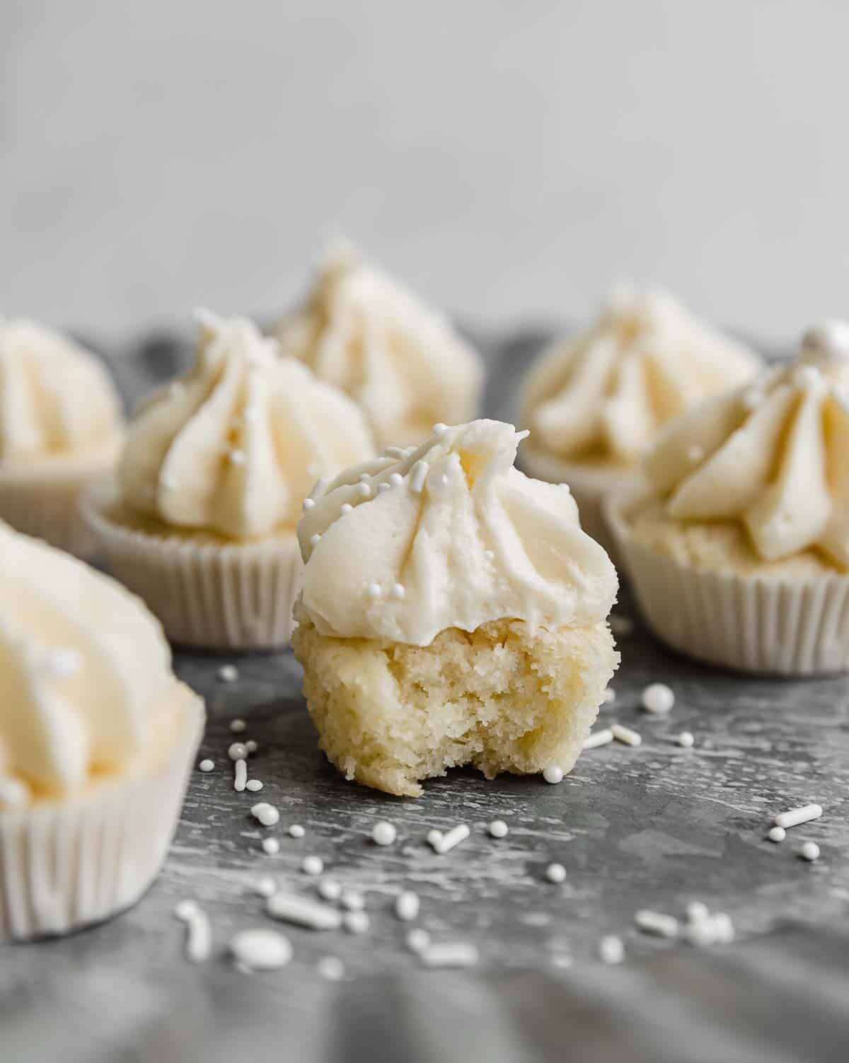 A vanilla mini cupcake topped with vanilla frosting with a bite taken out of the mini cupcake.