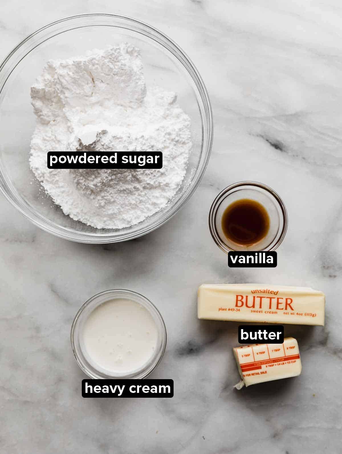 Vanilla cupcake frosting ingredients on a white background: powdered sugar, heavy cream, vanilla, butter.