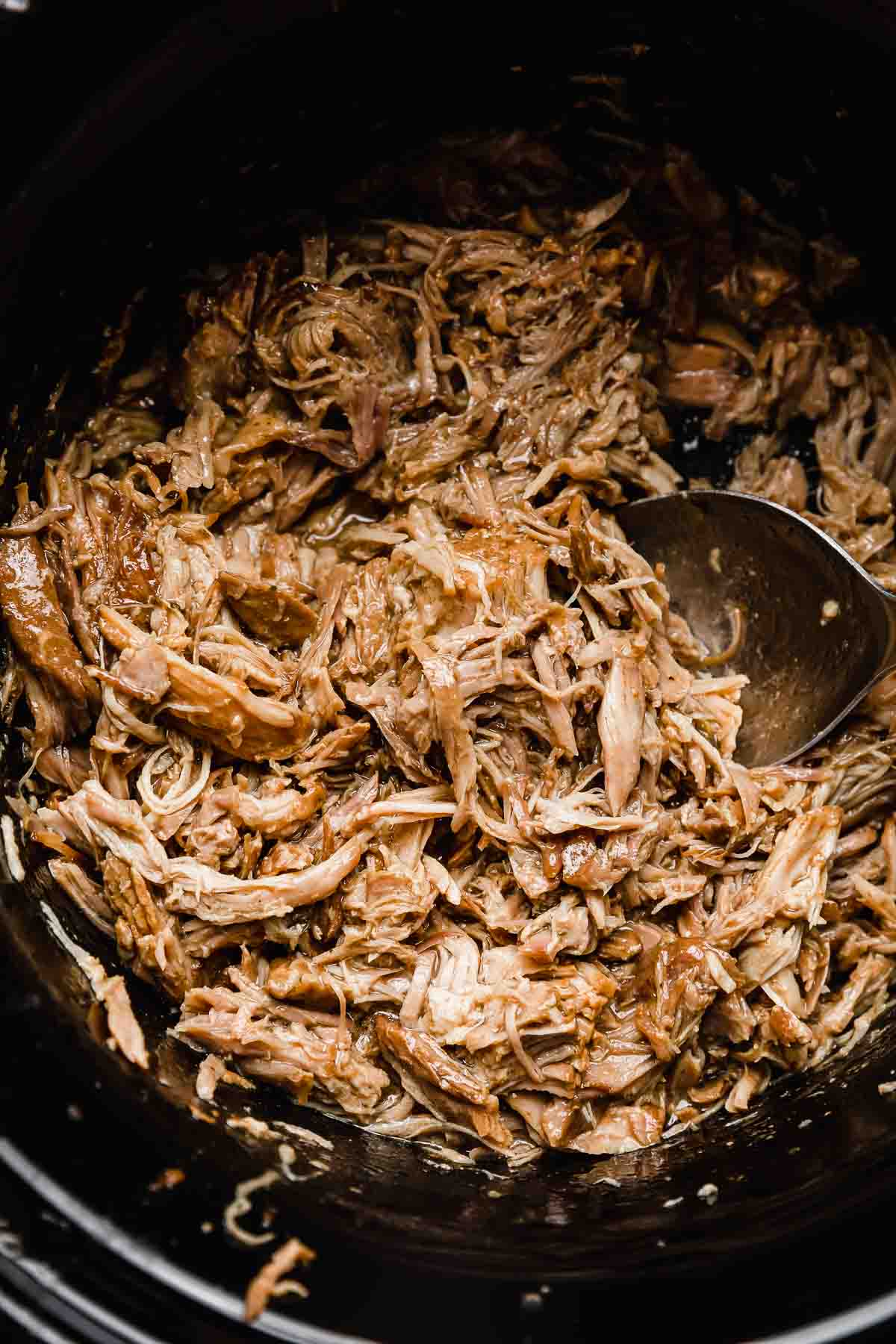 Close up photo of crock pot Mississippi Pork Roast meat in a black slow cooker.