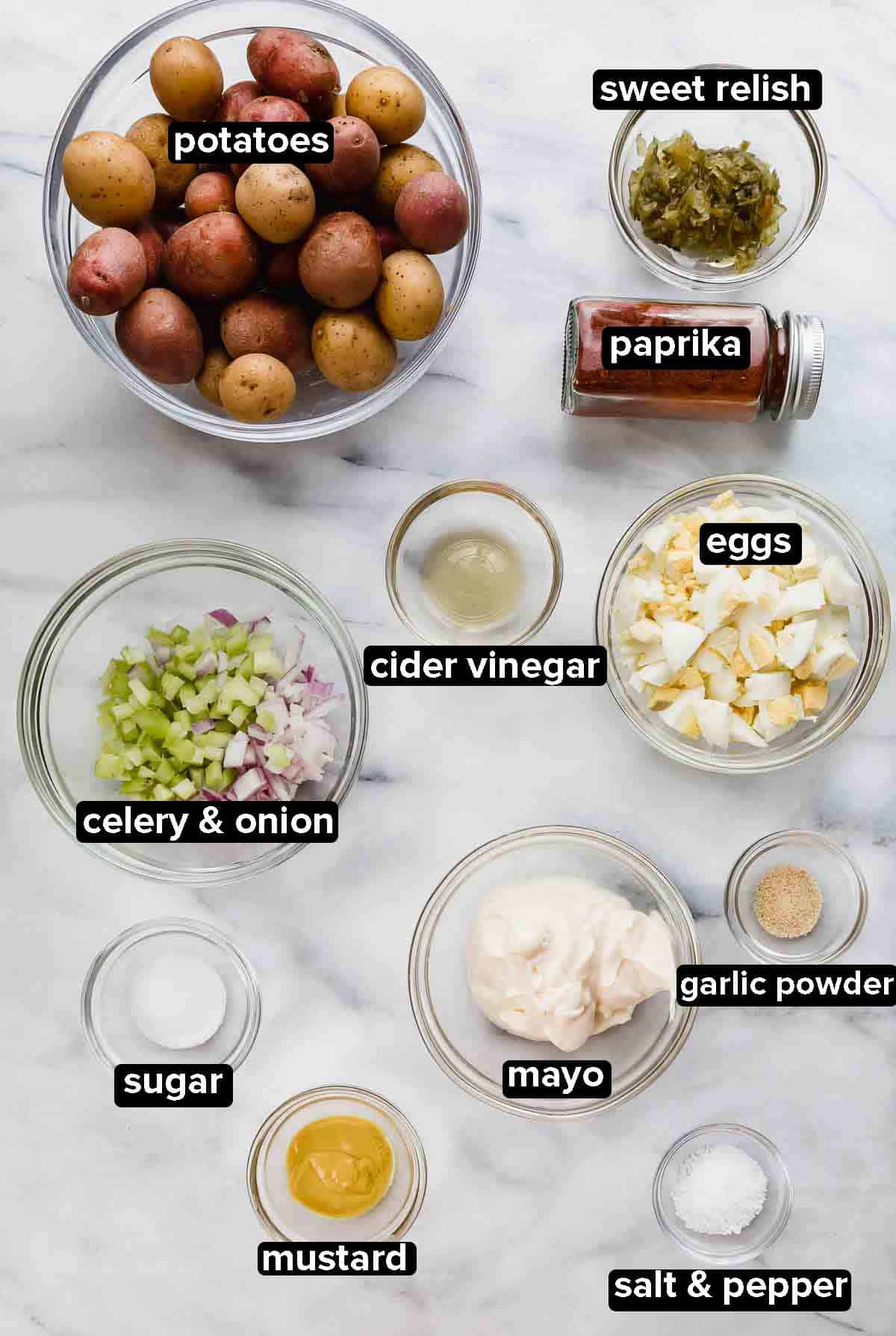 Baby Potato Salad ingredients in glass bowls: baby potatos, paprika, sweet relish, boiled eggs, sugar, mustard, mayo on a white background.