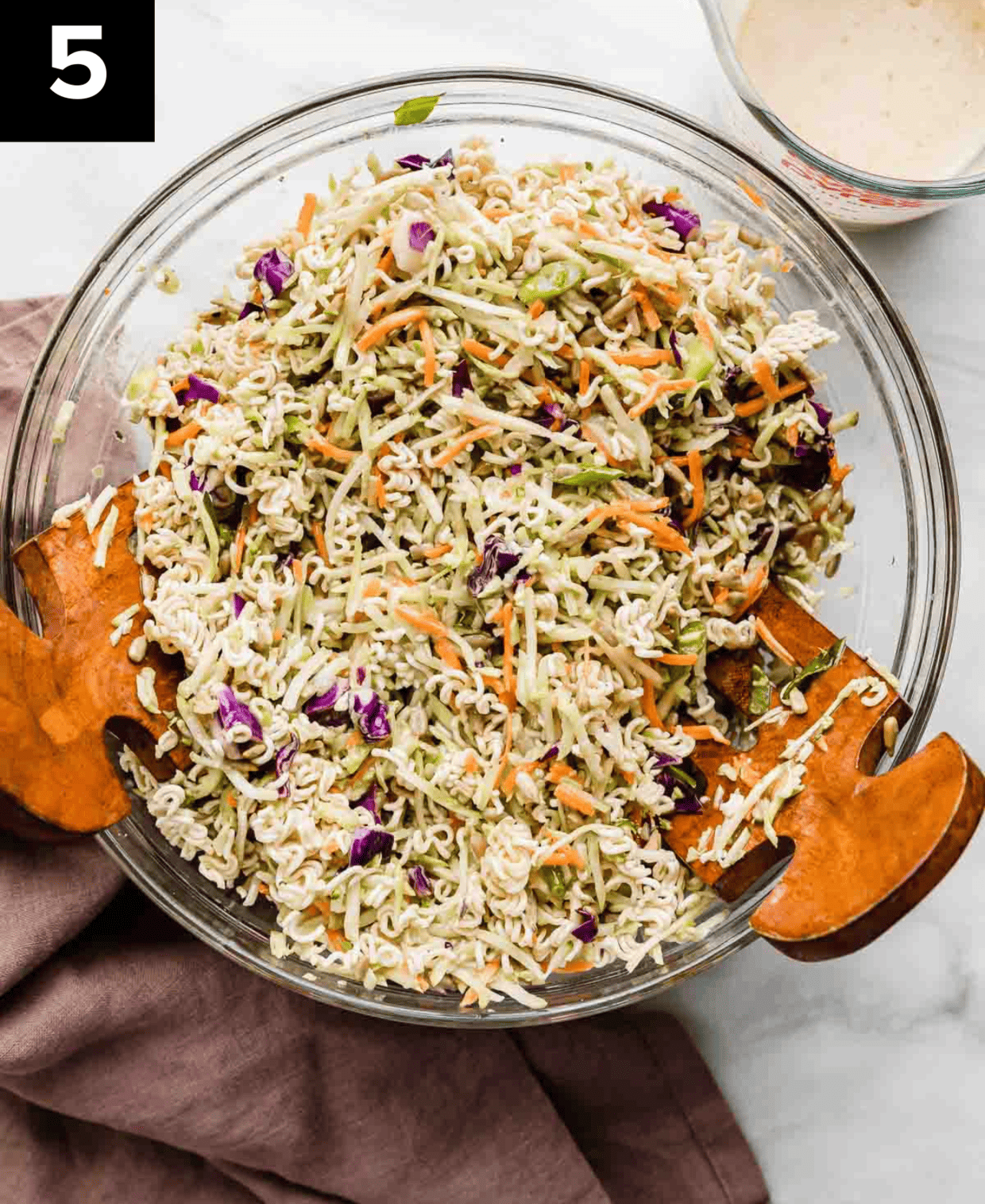 Asian Broccoli Slaw in a glass bowl with two wooden salad tongs.