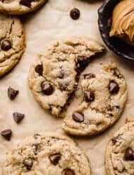 The best Peanut Butter Chocolate Chip Cookie on a Kraft parchment paper, split in half with a black bowl filled with peanut butter to the right of the cookie.