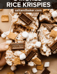 A hand grabbing a gooey S'more Rice Krispie Treats on Kraft colored paper with the words, "S'mores Rice Krispies" written in white font over the image.