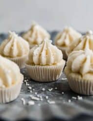 Mini vanilla cupcakes topped with vanilla frosting and white sprinkles, on a metal silver tray.