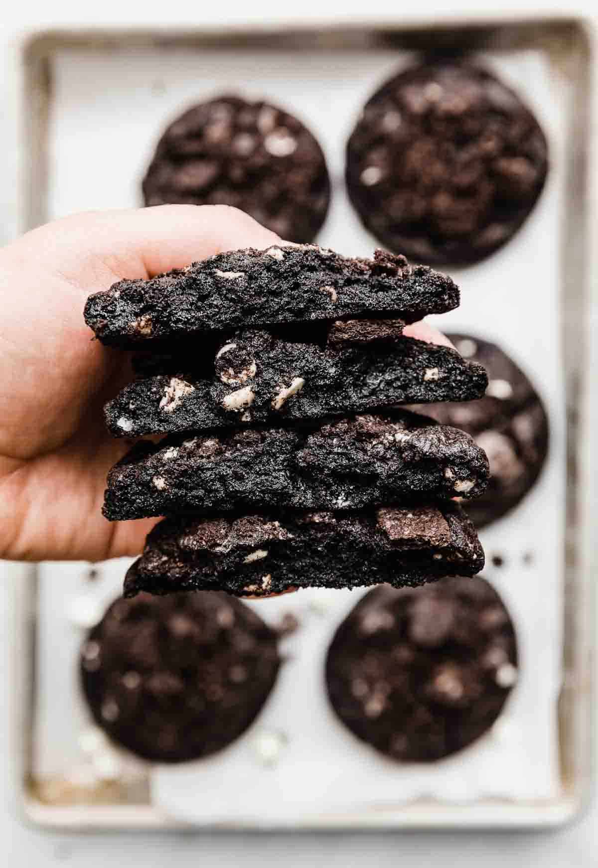 A crumbl copycat Chocolate Cookies and Cream Cookies cut in half with a hand holding up 4 halves of cookies.