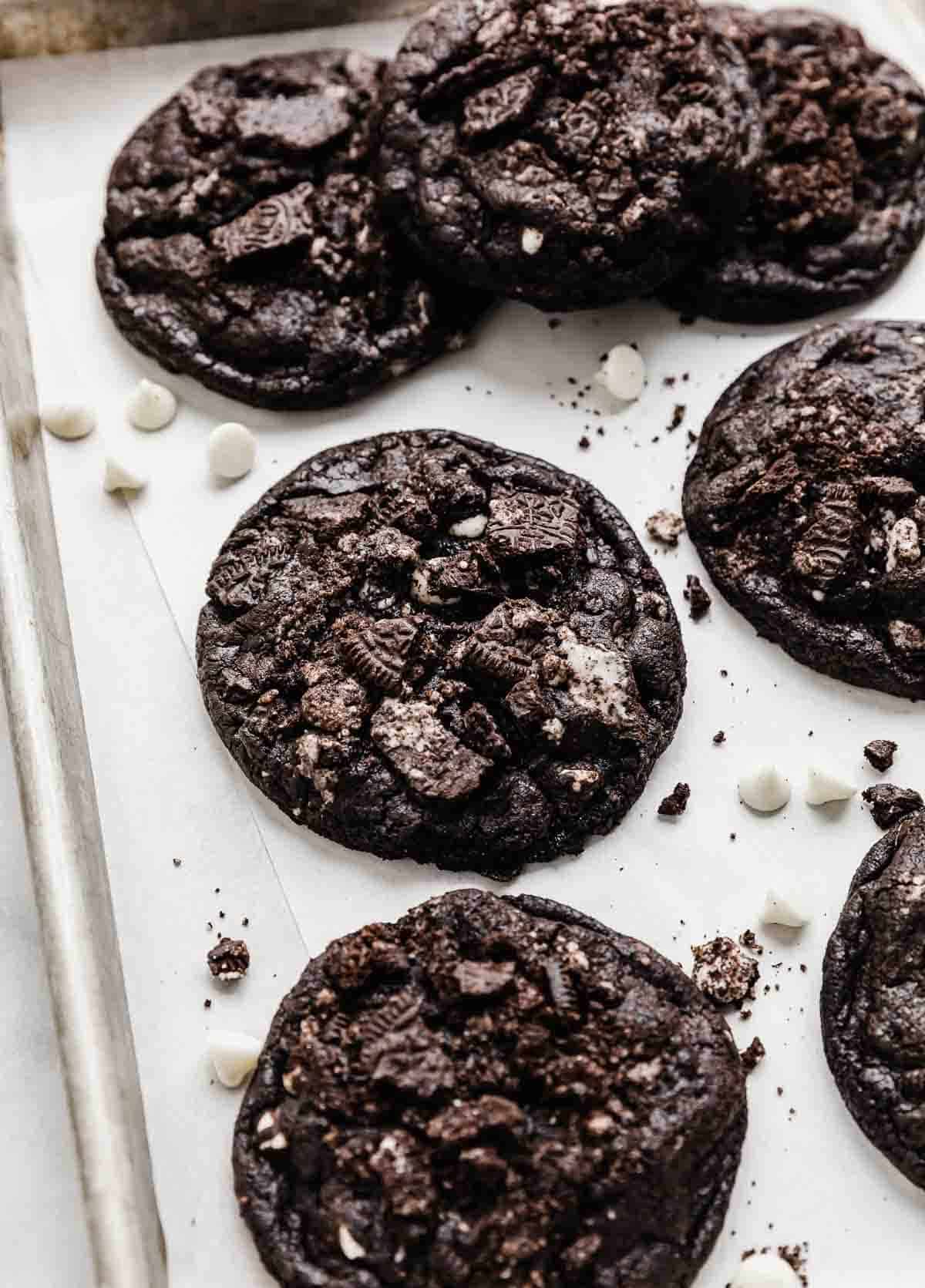 Chopped Oreo cookie topped chocolate cookies and cream cookies on a white parchment lined baking sheet.