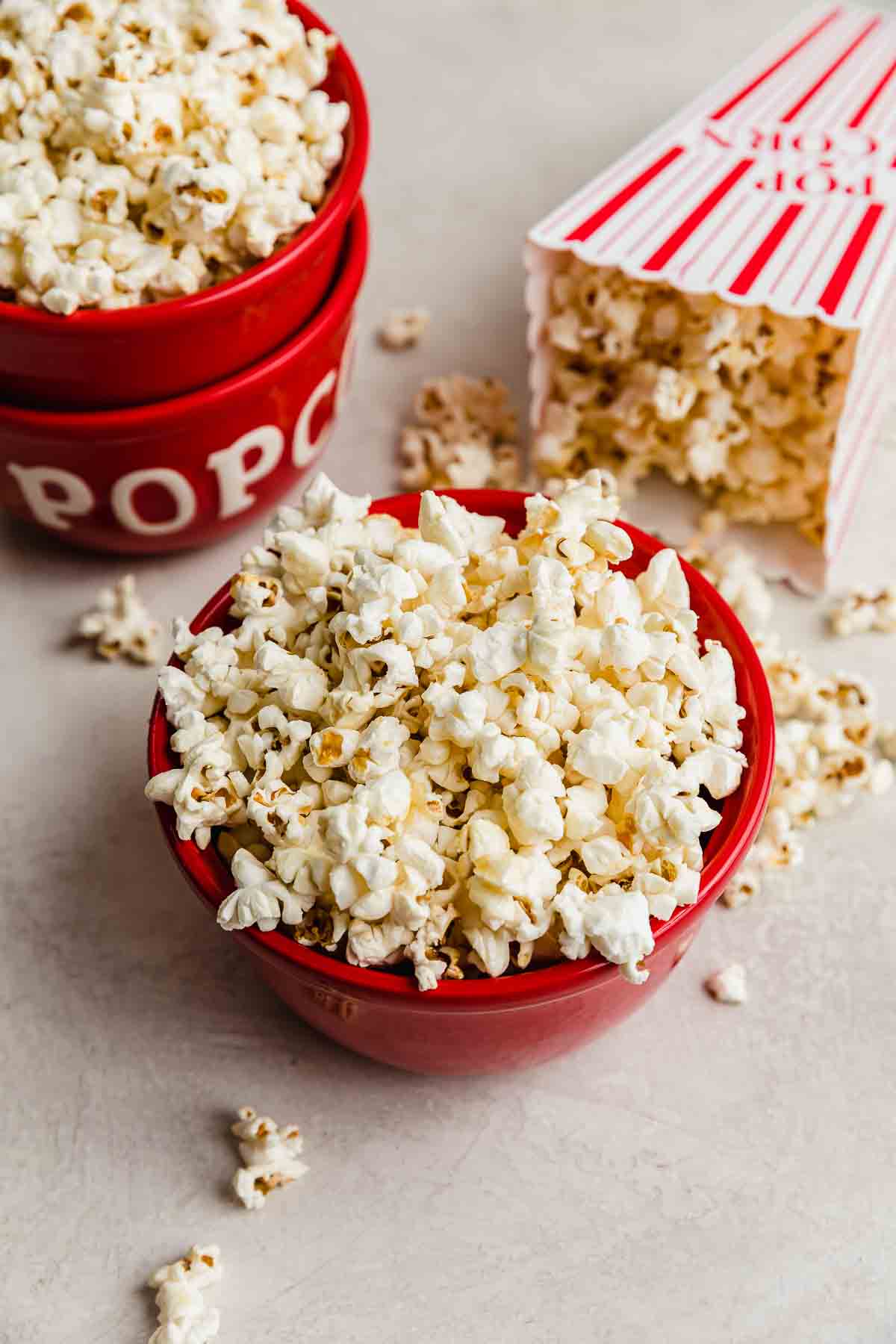 Kettle Corn Popcorn in a red bowl on a light gray background, with kettle corn surrounding the bowl.