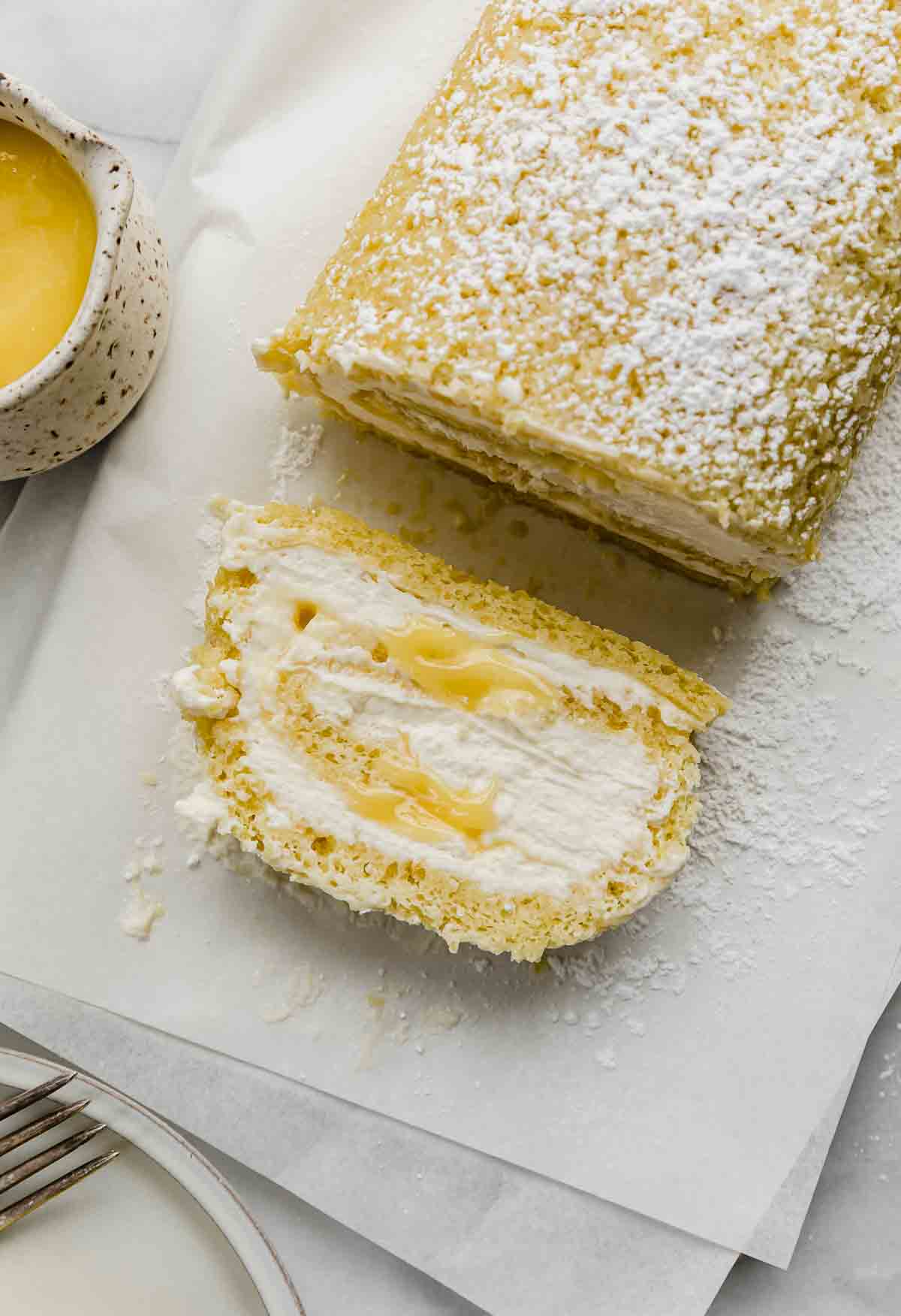 A slice of Lemon Swiss Roll filled with mascarpone cream and lemon curd, on a white parchment paper.