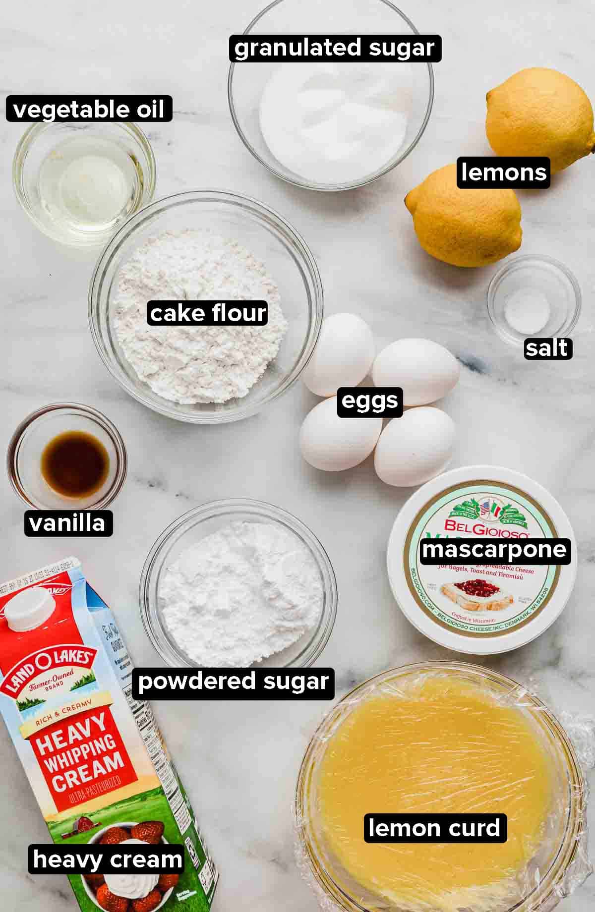 Lemon Swiss Roll ingredients on a white background: lemon curd, cake flour, lemons, sugar, eggs, vanilla, heavy cream, mascarpone cheese.