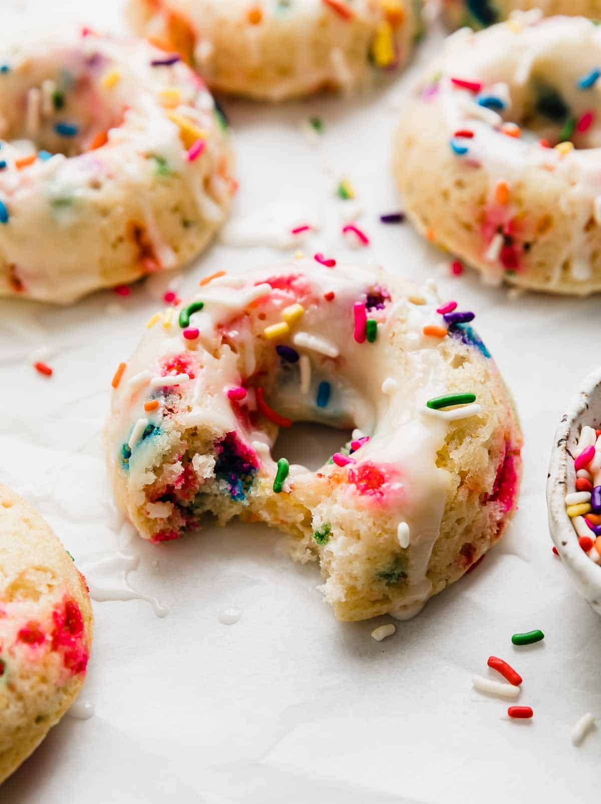 A sprinkle Donut with a bite taken out of it on a white background.