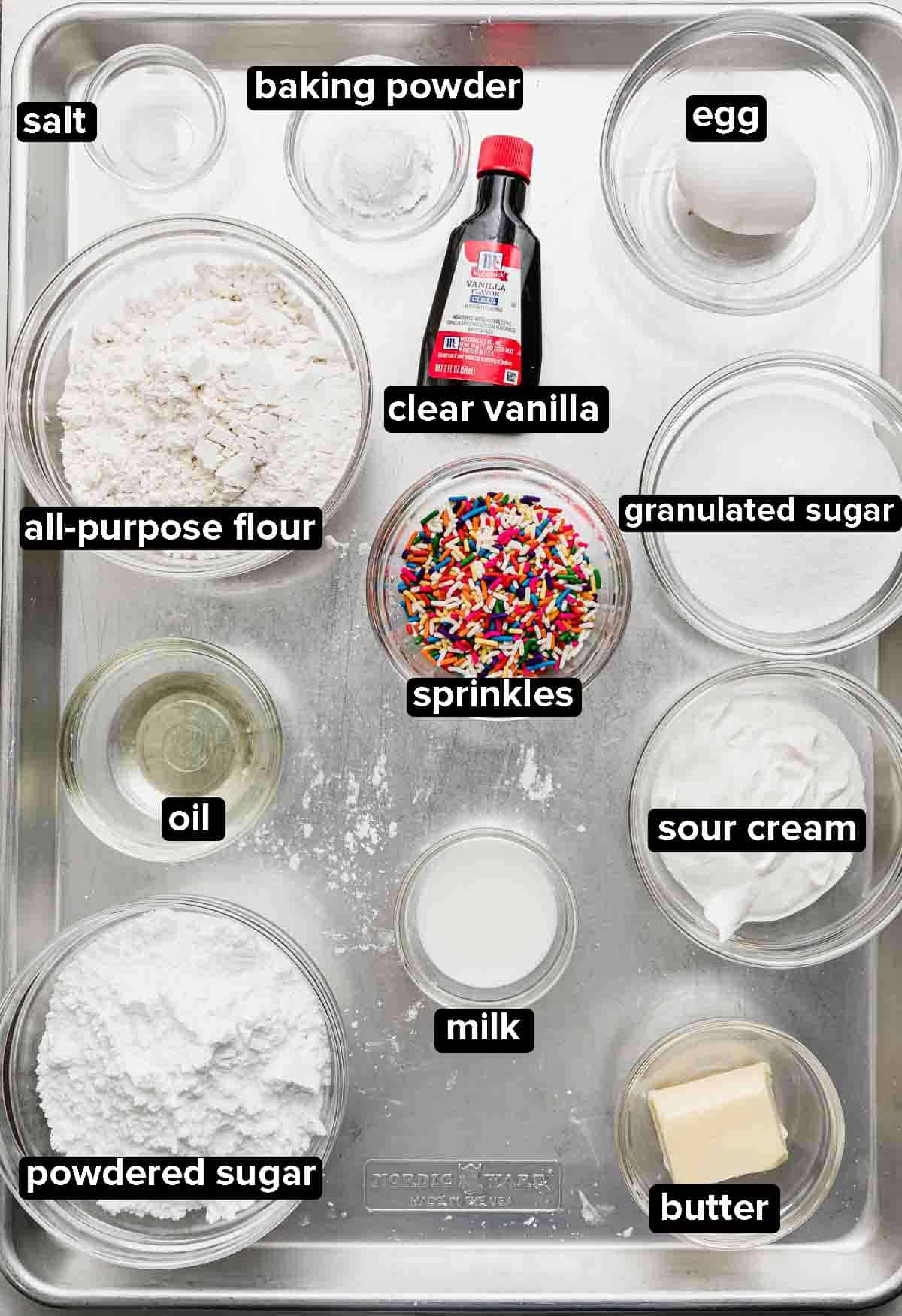 Sprinkle Donuts (funfetti donuts) ingredients portioned into glass bowls on a silver baking sheet.