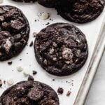 Chopped Oreo topped black cocoa cookies on a white parchment paper.