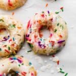 A Sprinkle Donut on a white background, the funfetti donut topped with glaze and extra sprinkles.