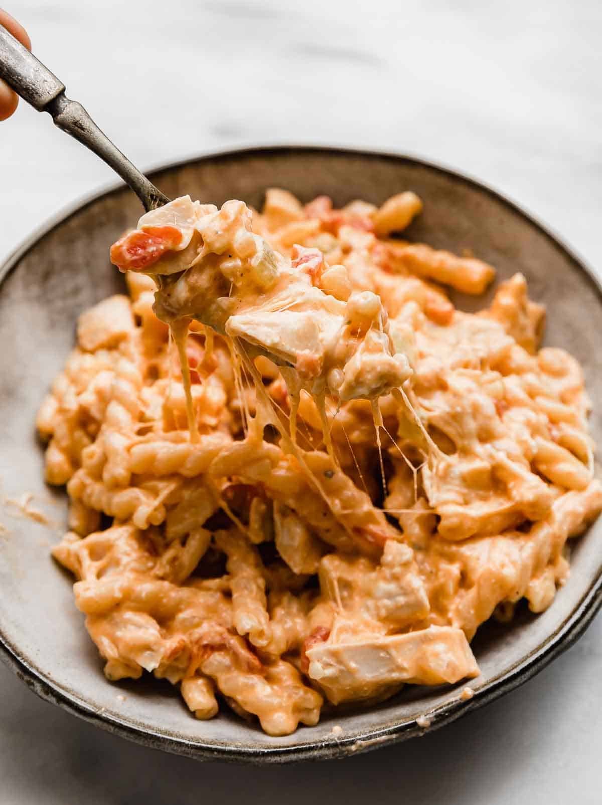 A gray bowl filled with cheesy Buffalo Chicken Pasta and a fork pulling up some of the pasta to show how cheesy it is.