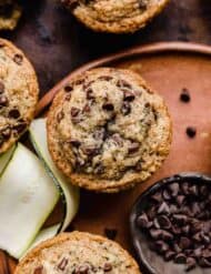 Mini chocolate chip topped Zucchini Chocolate Chip Muffins on a brown plate.