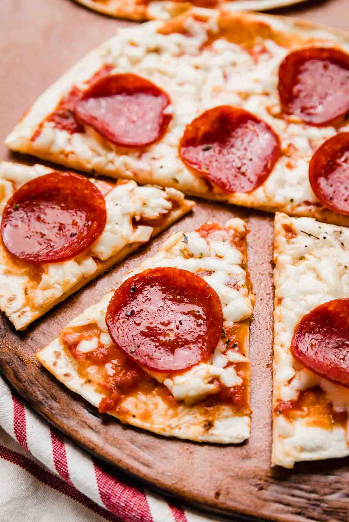 A Tortilla Pizza topped with pepperoni and sliced into triangles on a brown plate.