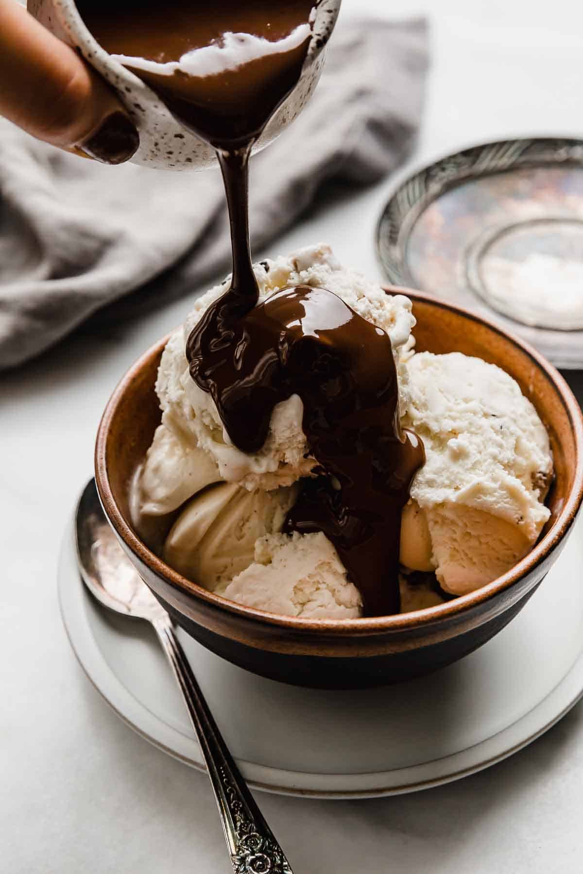 Magic Shell with coconut oil being poured overtop scoops of vanilla ice cream.