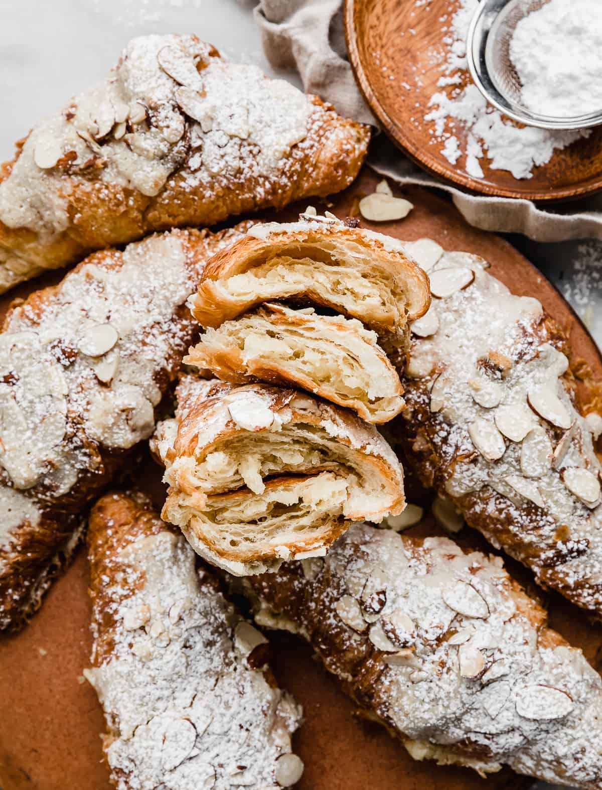 Homemade Almond Croissants split in half and surrounded by additional almond croissants on a brown plate.