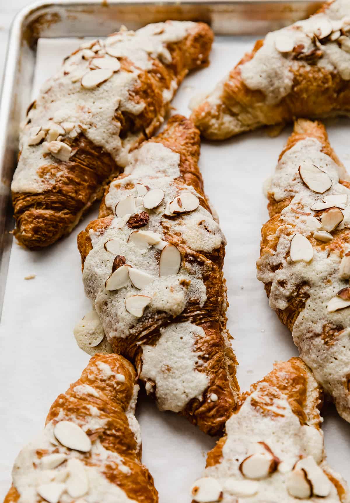 Almond Croissants on a white parchment paper covered baking sheet.