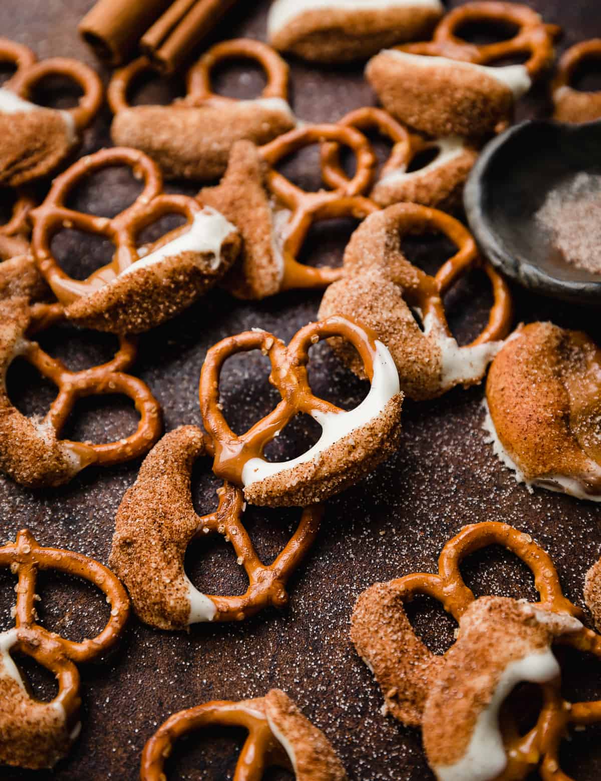 Snickerdoodle pretzels (half dipped pretzels in caramel, white chocolate, and cinnamon sugar) on a brown background. 