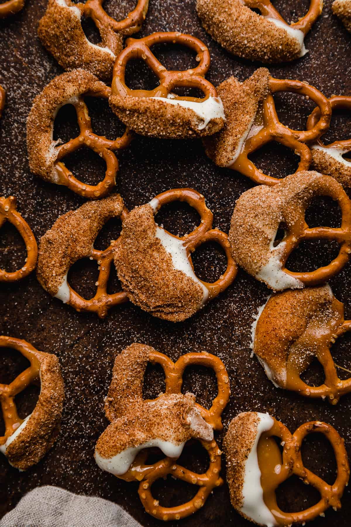 Pretzels coated in caramel, then white chocolate and a cinnamon sugar mixture on a brown background.