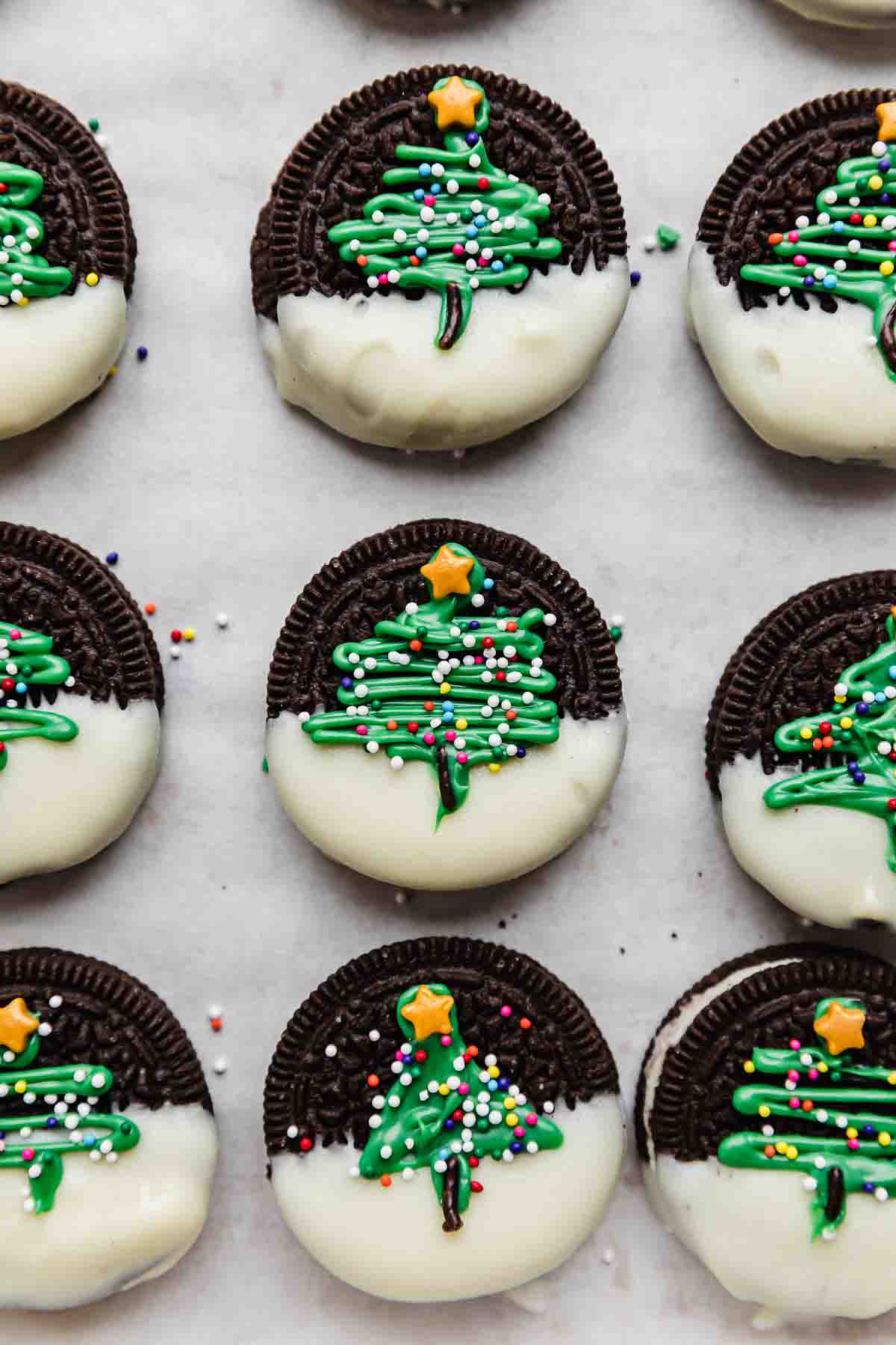 White parchment paper lined with Christmas Oreos (Christmas Trees piped onto half dipped white chocolate Oreos).